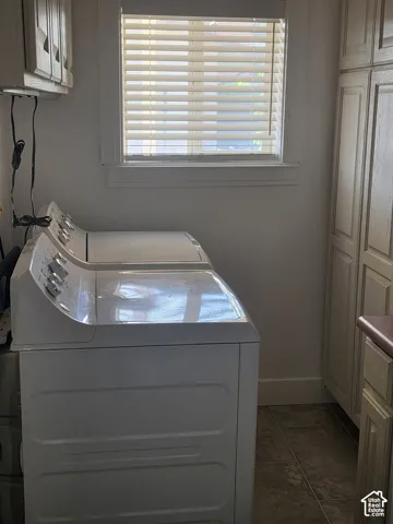 Laundry area featuring floor-to-ceiling built-in cabinetry, a window with horizontal blinds, and tile flooring