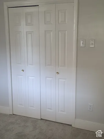 White bi-fold closet doors featuring a six-panel design and metallic knobs, paired with neutral carpeting