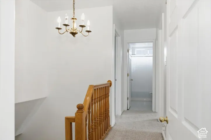 Hallway featuring neutral carpet, a five-arm metal chandelier, and a wood banister with vertical spindles