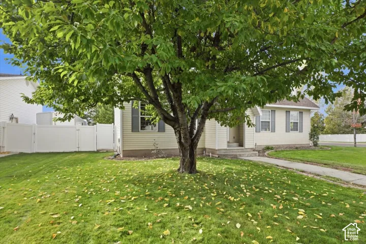 Vinyl siding exterior featuring decorative shutters, mature landscaping, concrete walkway, and white privacy fencing