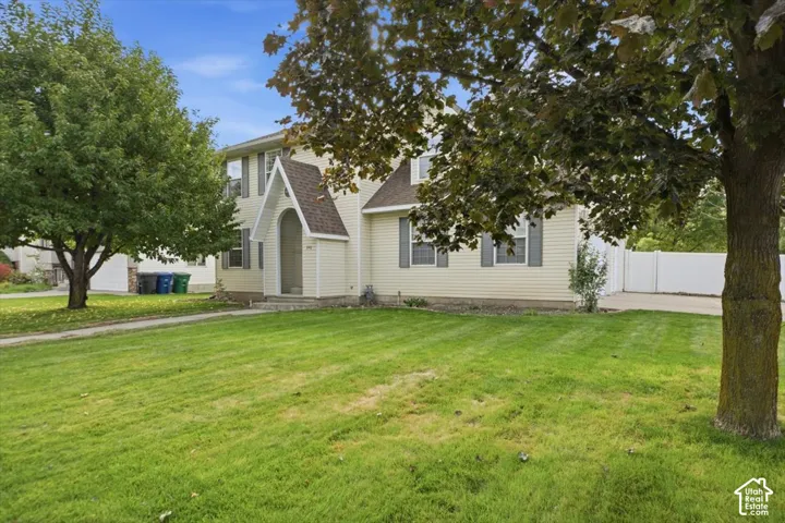 Two-story exterior featuring light-toned horizontal siding, a covered arched entryway with a steep roofline, gray window shutters, and a concrete driveway