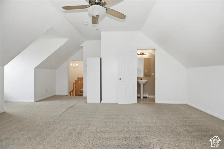 Vaulted ceiling room featuring neutral carpeting, a central ceiling fan with integrated lighting, and a pedestal sink with a wall-mounted light fixture