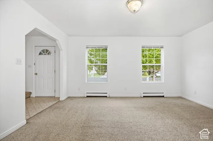 Neutral interior featuring wall-to-wall carpeting, two grid-pattern windows, an arched entryway, and a white exterior-style door with a half-moon glass insert