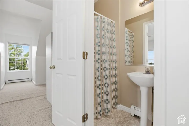 Bright ensuite bathroom featuring a pedestal sink, mosaic tile shower surround with coordinating curtain liner, and neutral stone-finish flooring