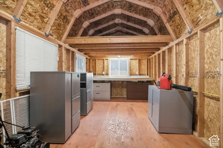 Outbuilding featuring a gambrel roofline, exposed wood-stud framing, plywood flooring, dual horizontal sliding windows, and interior wooden rafters