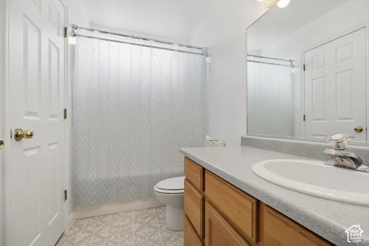 Bathroom featuring a vanity with wood-finish cabinetry, a solid-surface countertop with an integrated basin, a large wall-mounted mirror, and a combination tub and shower enclosure