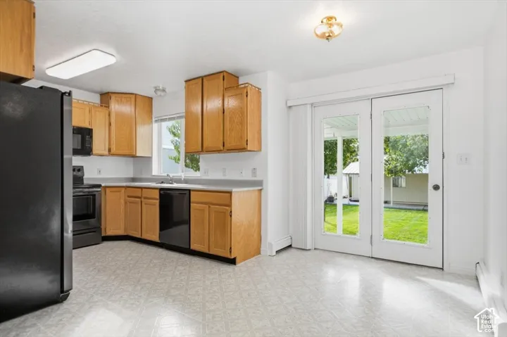 Kitchen featuring wood cabinetry, integrated black appliances, light-toned laminate flooring, and dual-pane glass patio doors