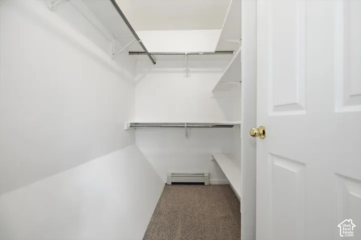 Walk-in closet featuring tiered white shelving, integrated metal clothing rods, and carpeting