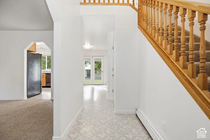 Foyer featuring geometric patterned flooring, carpeted staircase with wood railing, and glass-paneled double doors