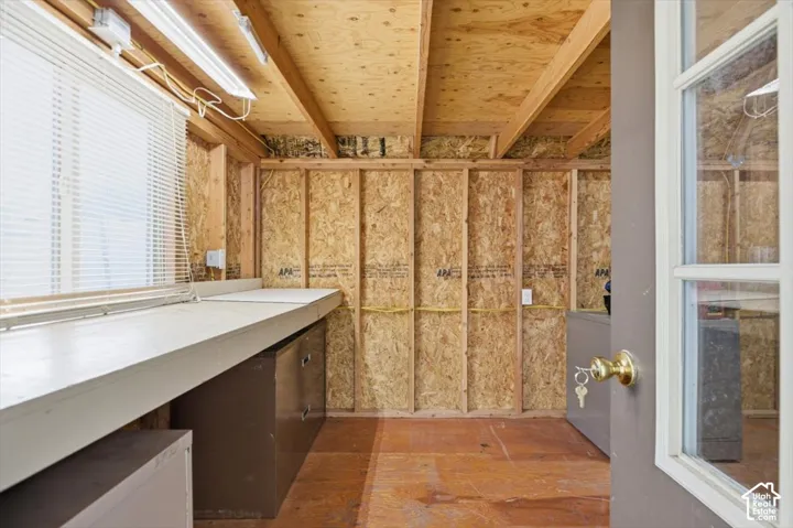 Utility space featuring exposed wood-stud framing, a built-in workbench, overhead fluorescent lighting, and a window with integrated blinds