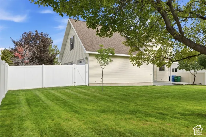 Expansive backyard featuring a level lawn, white vinyl fencing, concrete patio, and mature trees