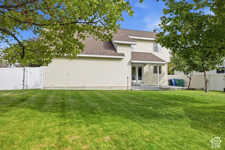 Backyard featuring a manicured lawn, white vinyl fencing, concrete patio, and mature trees
