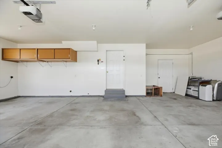 Multi-car garage featuring smooth concrete flooring, overhead storage cabinetry, automated door opener, and two egress doors