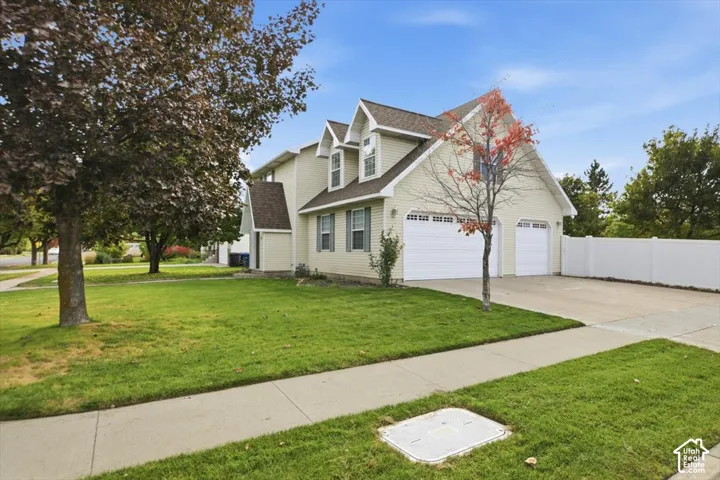 Two-story residence featuring light-colored horizontal siding, dual dormer windows, a two-car garage, and a white privacy fence