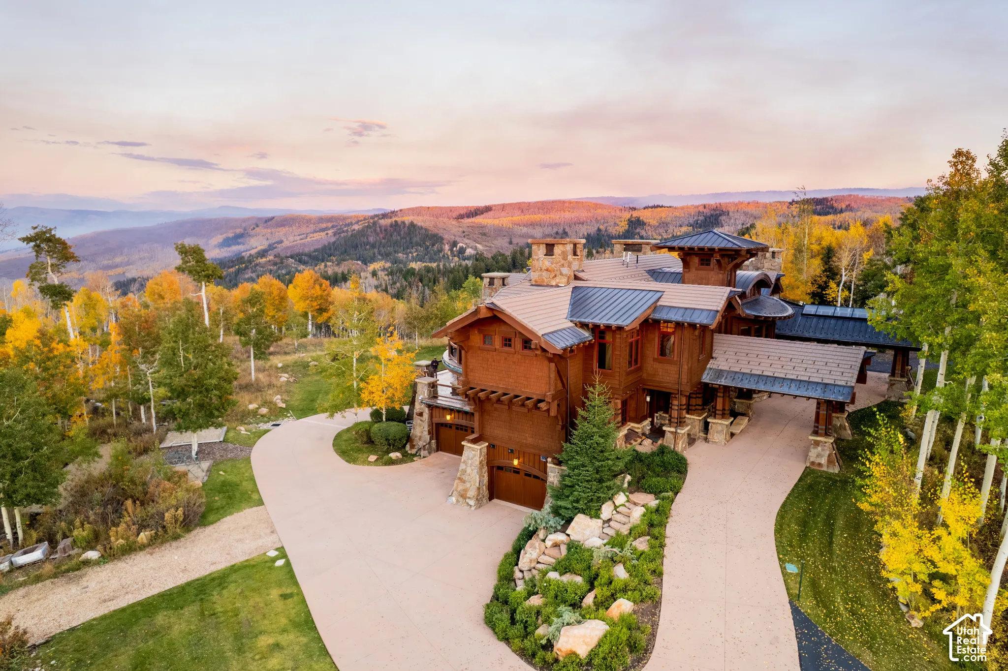 Mountain estate featuring shingle and wood siding, stone masonry accents, a metal roof, and a paved multi-car driveway, set against a backdrop of mountainous terrain