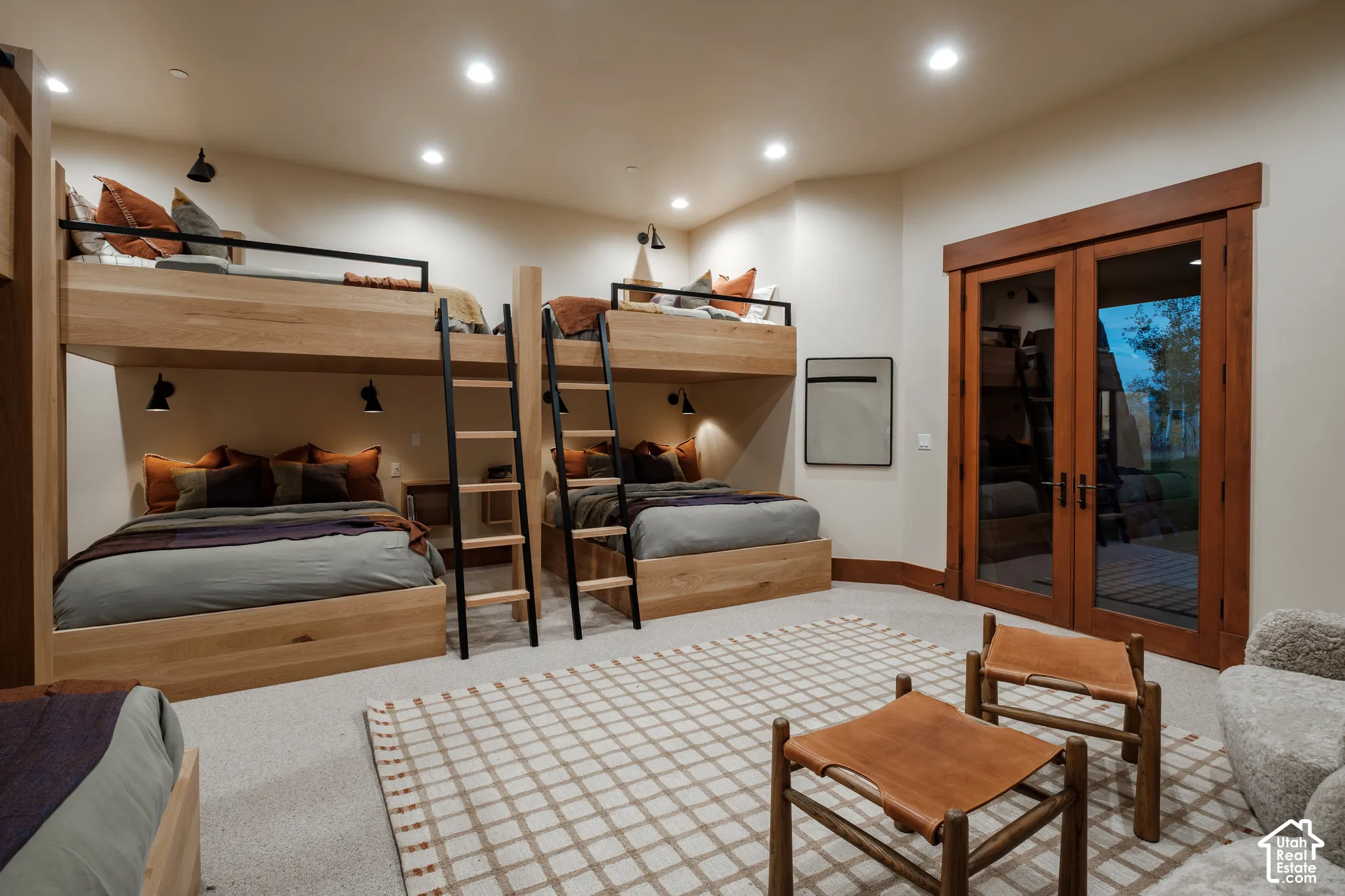 Custom built-in wood bunk beds featuring integrated metal ladders and matte black wall-mounted lighting, recessed ceiling lighting, and wood-framed glass double doors