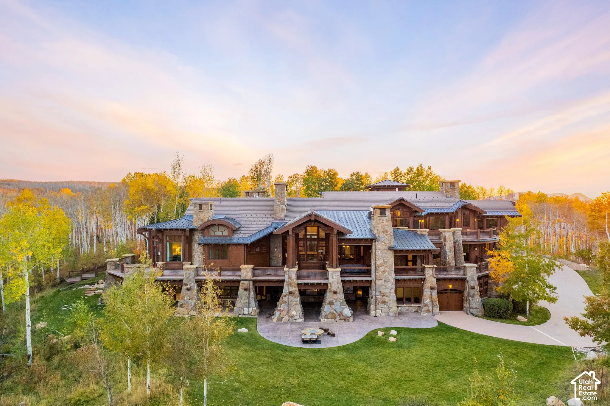 Mountain-style estate featuring natural stone exterior cladding, exposed timber framing, multiple covered balconies, metal roofing, and a circular concrete driveway