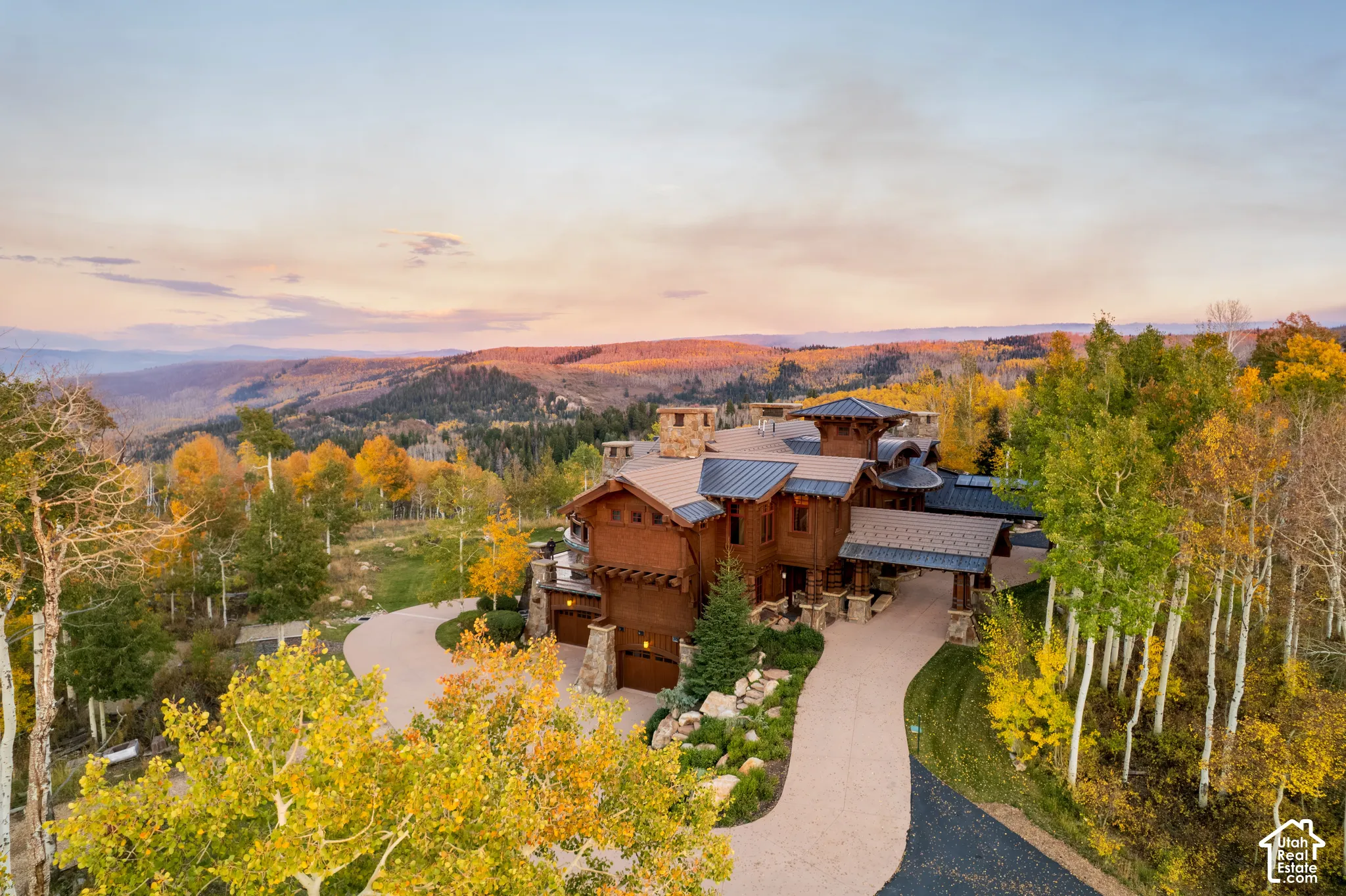 Multi-level mountain residence featuring stone and wood-shake exterior cladding, standing-seam metal roofing, expansive stone chimney stacks, and a winding paved motor court