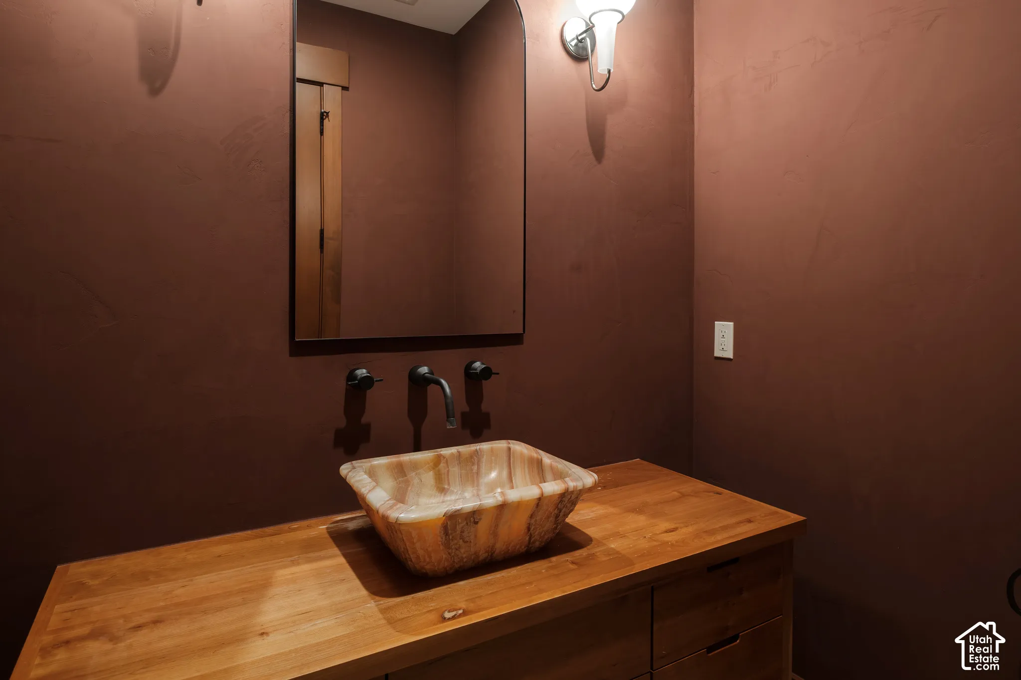 Wood vanity cabinet with a natural wood countertop, rectangular vessel sink, wall-mounted matte black faucet, and arched mirror