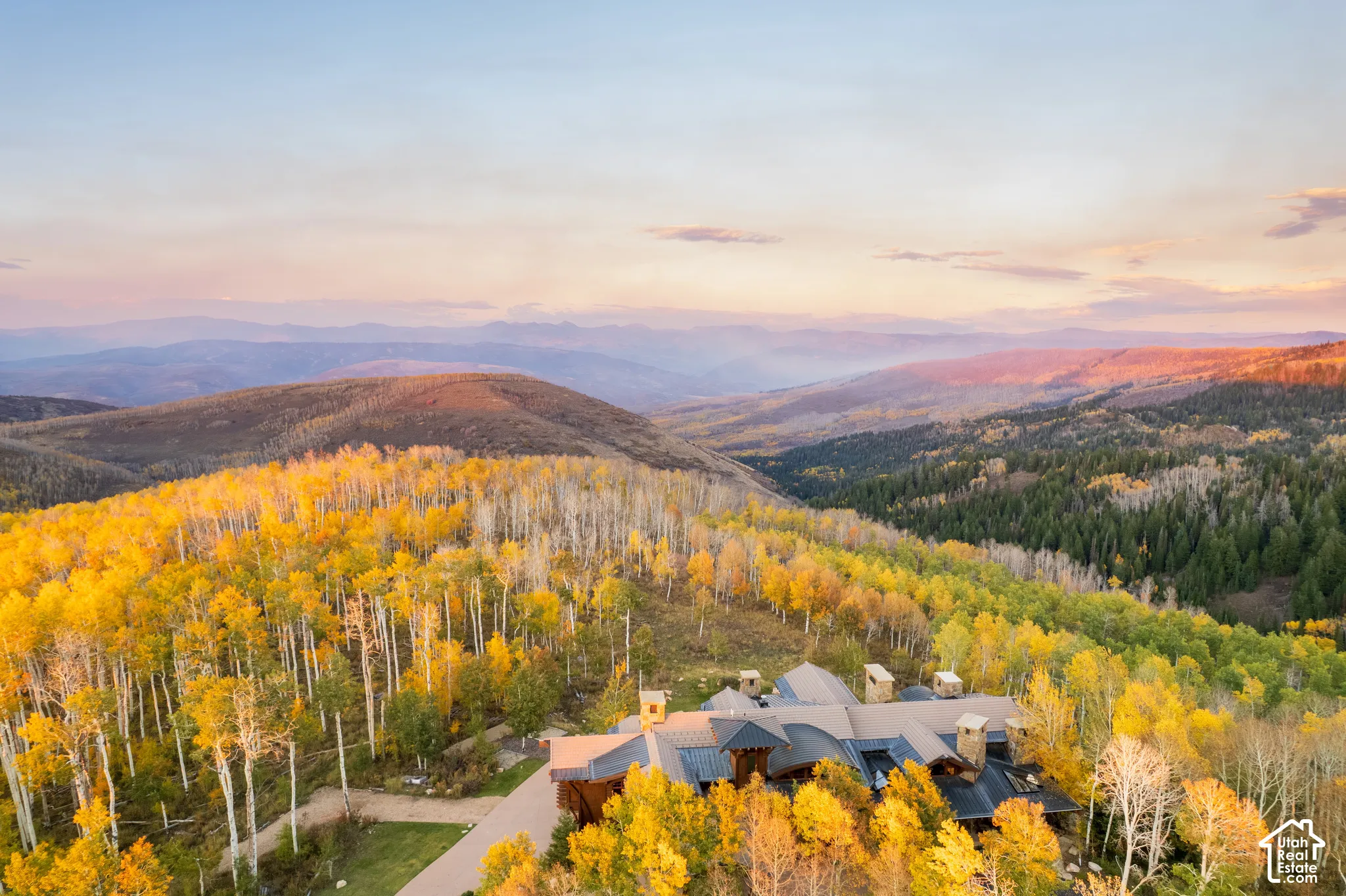 Mountain estate featuring a metal roof, stone chimneys, and a private paved driveway, situated amidst a forest of mature aspen and pine trees with expansive ridgeline scenery