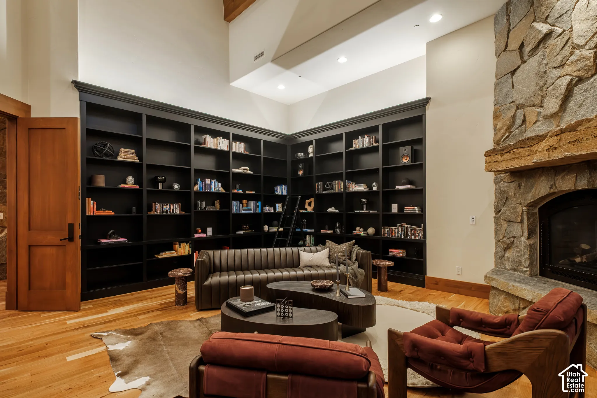 Floor-to-ceiling built-in shelving, natural stone fireplace with a substantial timber mantel, vaulted ceiling, and wood-finish flooring