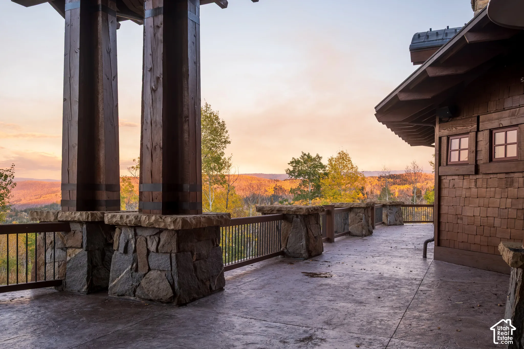 Expansive exterior terrace featuring rustic stone-base timber columns, decorative metal railings, shingle-style siding, and mountain horizon scenery