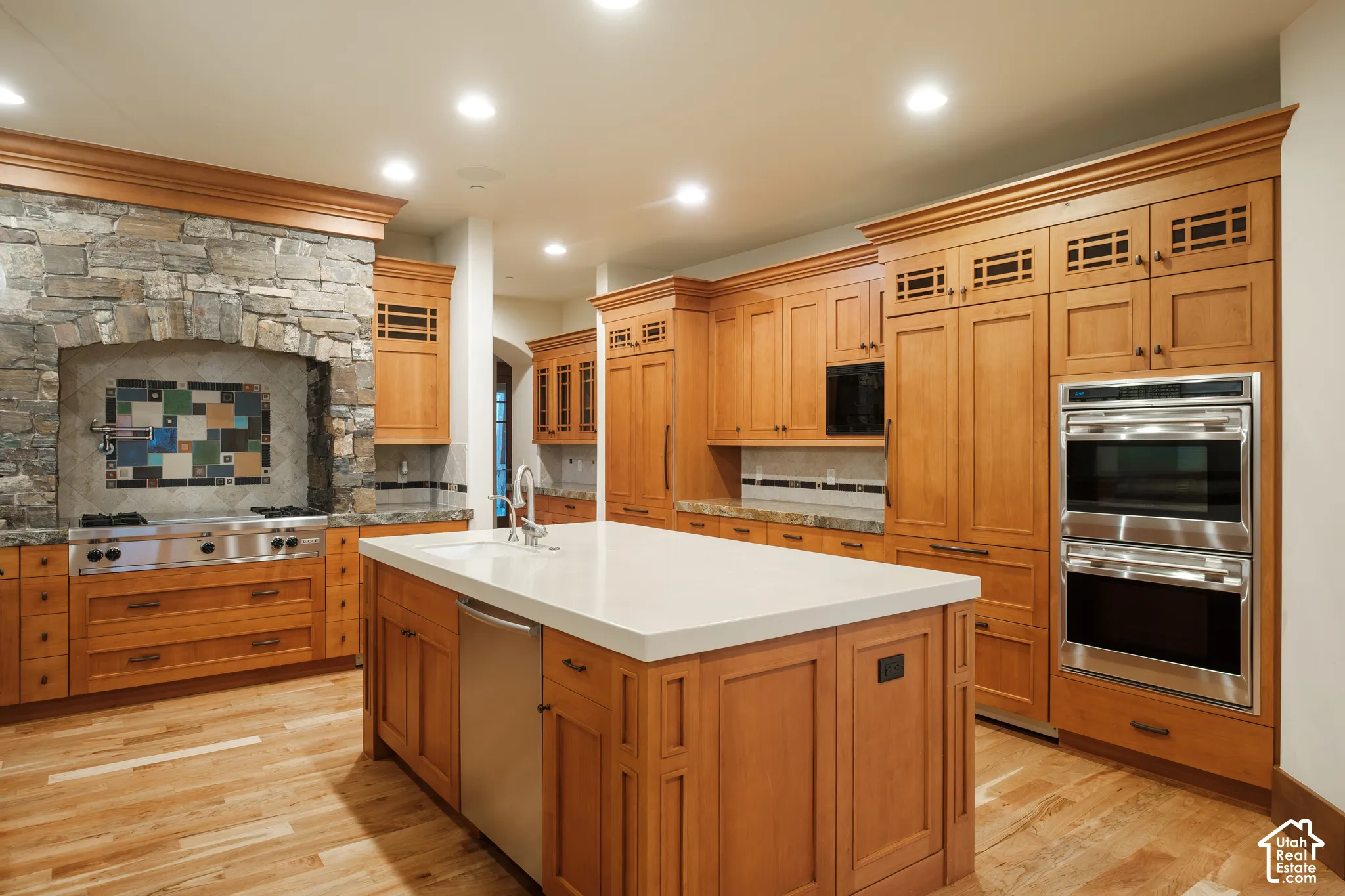 Kitchen featuring custom wood cabinetry, a central island with quartz countertop, integrated stainless steel appliances, a stone-surround cooktop alcove with mosaic tile backsplash, and wood-finish flooring