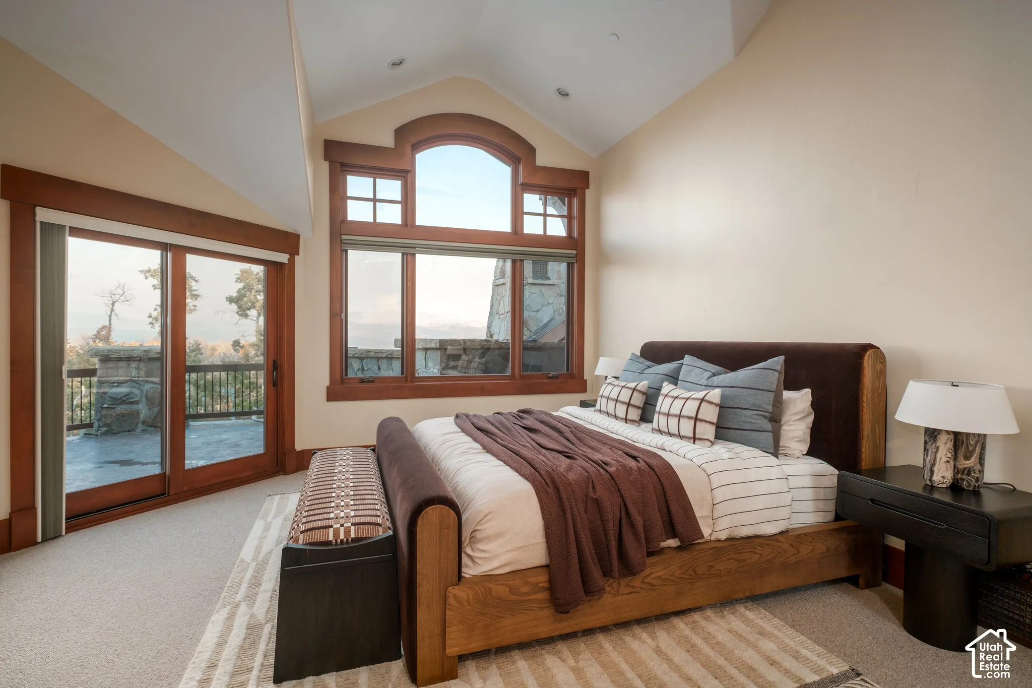 Vaulted ceiling with recessed lighting, prominent arched-top window, wood-trimmed window casings, and glass slider with access to a stone-paved exterior deck