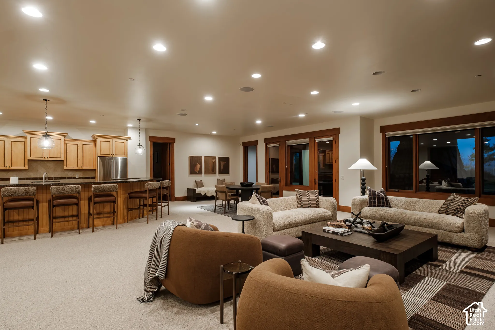 Open-concept interior featuring light wood cabinetry, a built-in kitchen island with counter seating, recessed lighting, and large paneled windows with wood trim