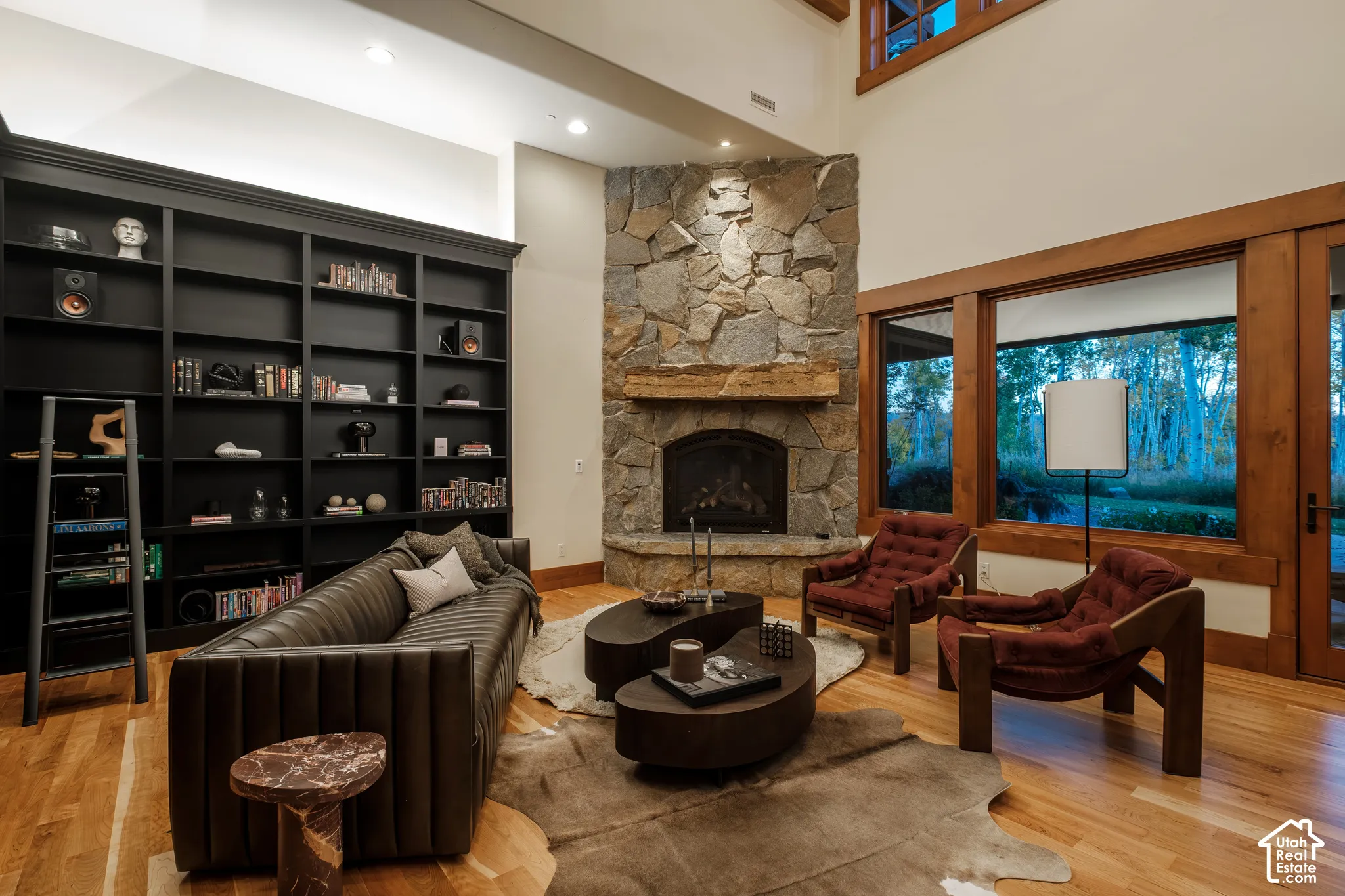 Double-height ceiling, corner fireplace with floor-to-ceiling stone surround, heavy timber mantel, built-in floor-to-ceiling black cabinetry, and hardwood flooring