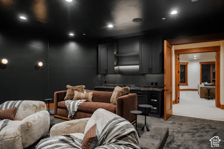 Custom built-in cabinetry with integrated under-cabinet lighting, dark stone countertop, built-in beverage refrigerator, recessed ceiling lighting, and wall-mounted spherical sconces