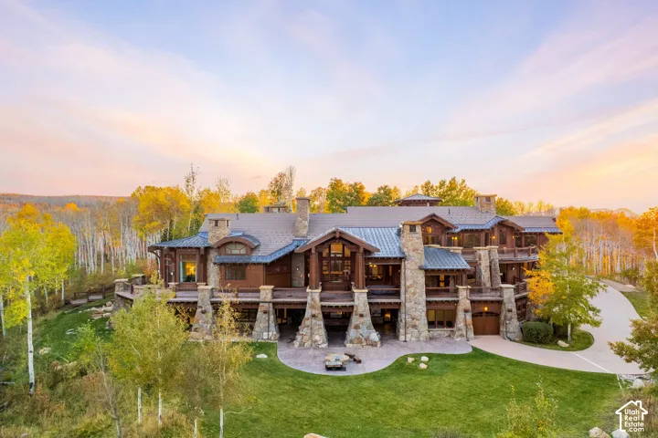 Mountain-style estate featuring natural stone exterior cladding, exposed timber framing, multiple covered balconies, metal roofing, and a circular concrete driveway