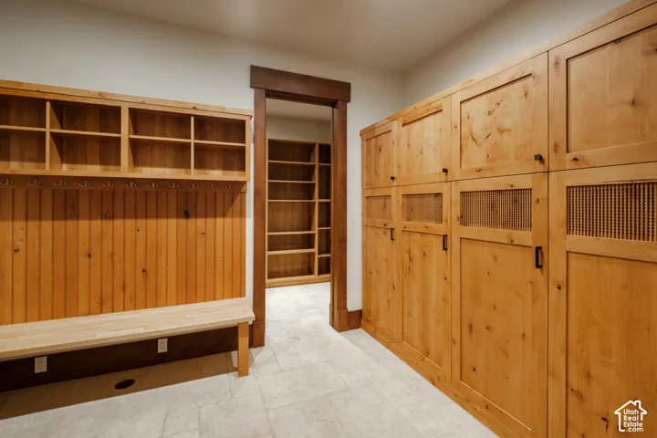 Custom wood cabinetry featuring integrated storage lockers with mesh paneling, open upper shelving, built-in wooden bench seating, and stone tile flooring