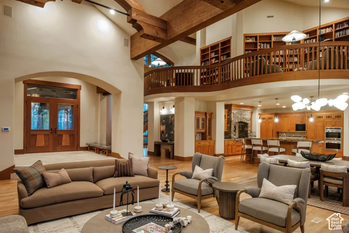 Double-height vaulted ceilings with exposed timber beams, built-in wooden shelving, a wraparound wood-railed mezzanine, and double-door entryway
