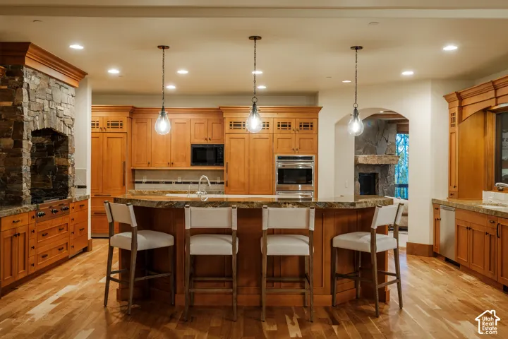 Kitchen featuring custom wood cabinetry, natural stone-faced range alcove, multi-level stone countertop, integrated stainless steel appliances, and wood-finish flooring