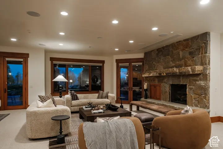 Floor-to-ceiling stone fireplace with a thick timber mantel and raised stone hearth, natural wood window and door casings, and recessed ceiling lighting