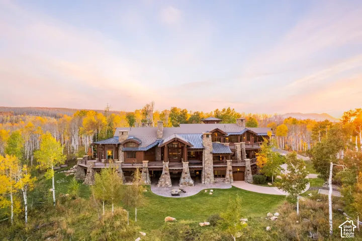 Custom mountain estate featuring heavy timber frame construction, multi-level exterior stone masonry, metal roofing, expansive wraparound decking, and integrated stone chimneys