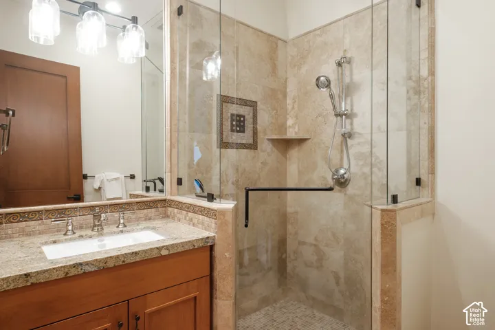 Stone tile walk-in shower with a glass enclosure and handheld fixture, wood vanity, stone countertop with an integrated basin, and three-light wall-mounted vanity fixture