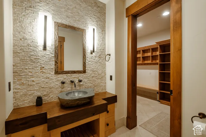 Stacked stone accent wall with dual wall-mounted sconces, custom wood vanity featuring a natural stone vessel sink, and built-in wood shelving units