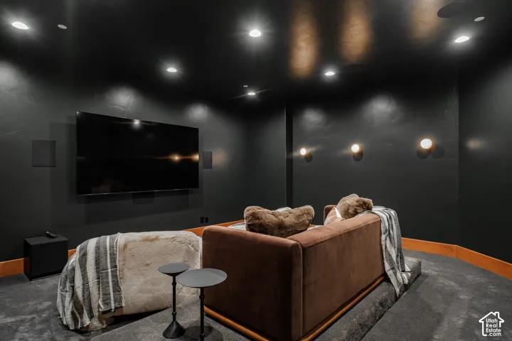 Enclosed room featuring dark matte wall finishes, recessed ceiling lighting, wall-mounted globe sconces, wood-trim detailing, and tiered flooring