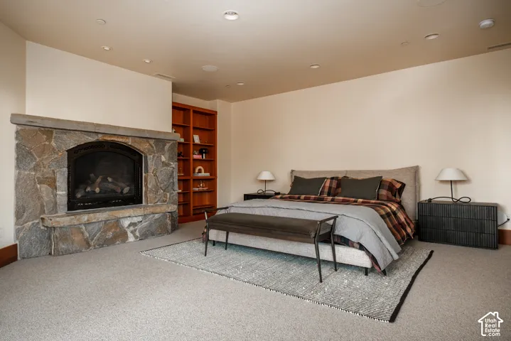 Floor-to-ceiling stone fireplace surround, built-in wooden shelving, recessed lighting, and neutral carpeting