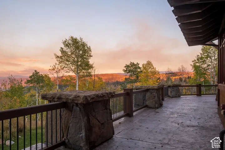 Expansive exterior deck featuring stone-clad pillars, metal balustrades, and a covered section with wood-beam accents