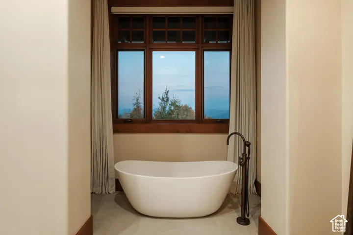 Freestanding soaking tub with a floor-mounted dark metal faucet, positioned before a multi-pane window with dark wood trim and mountain scenery