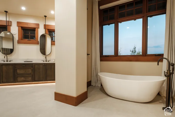 Freestanding soaking tub with a floor-mounted bronze-finish faucet, dual-sink vanity featuring stone countertops, oval wall-mounted mirrors, and extensive natural wood trim throughout