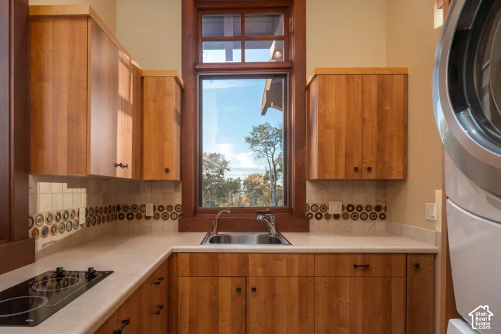 Custom wood cabinetry, stone countertops, decorative tile backsplash, undermount sink with chrome fixtures, and a glass cooktop