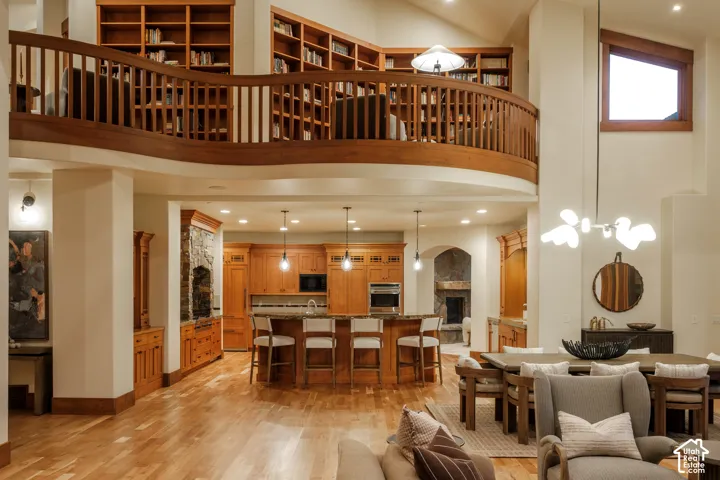 Expansive open-concept interior featuring wood-finish flooring, a curved wood-railing mezzanine, floor-to-ceiling custom built-in bookshelves, and a kitchen with wood cabinetry and stone countertops