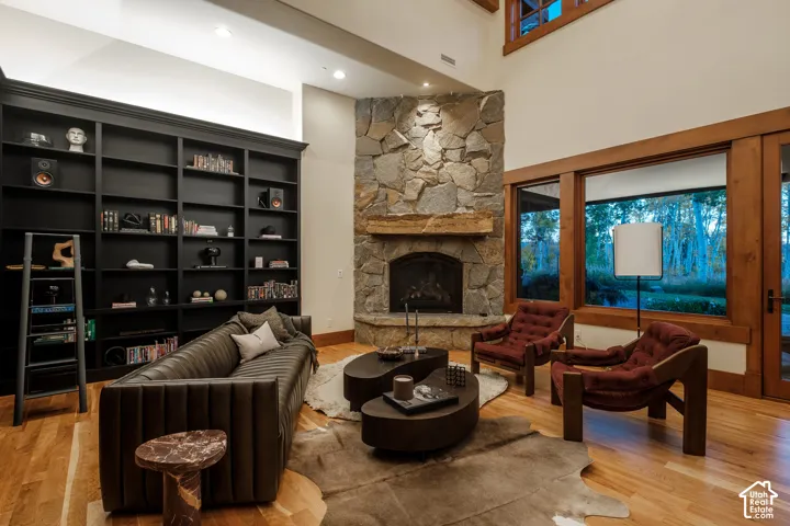 Double-height ceiling, corner fireplace with floor-to-ceiling stone surround, heavy timber mantel, built-in floor-to-ceiling black cabinetry, and hardwood flooring