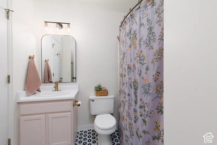 Bathroom featuring a vanity with a white countertop and gold-toned faucet, arched mirror, three-light wall fixture, and patterned floor tile
