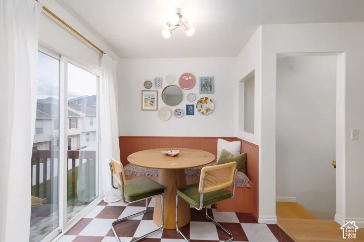 Built-in L-shaped bench seating with paneled wainscoting, checkerboard tile flooring, sliding glass door, and multi-bulb semi-flush mount lighting