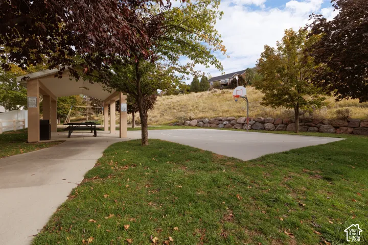 Outdoor recreational area featuring a concrete basketball court, covered pavilion, landscaped lawn, and stone retaining wall